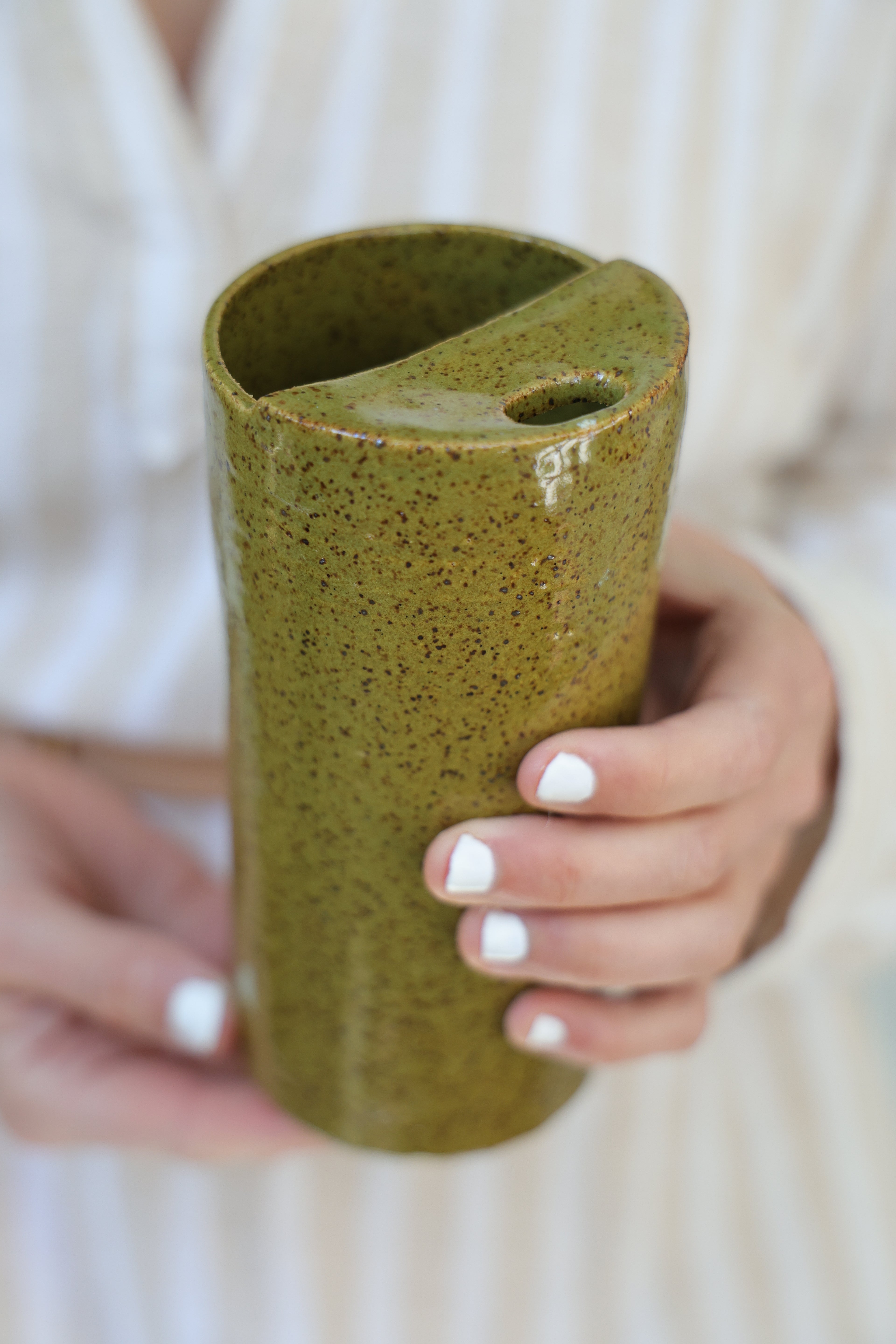 Person holding an olive green ceramic cylindrical travel cup with speckles