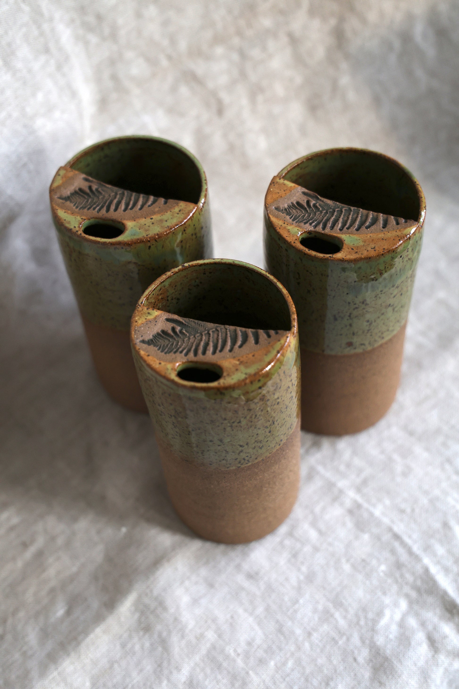 Three ceramic containers with fern patterns on a white fabric background
