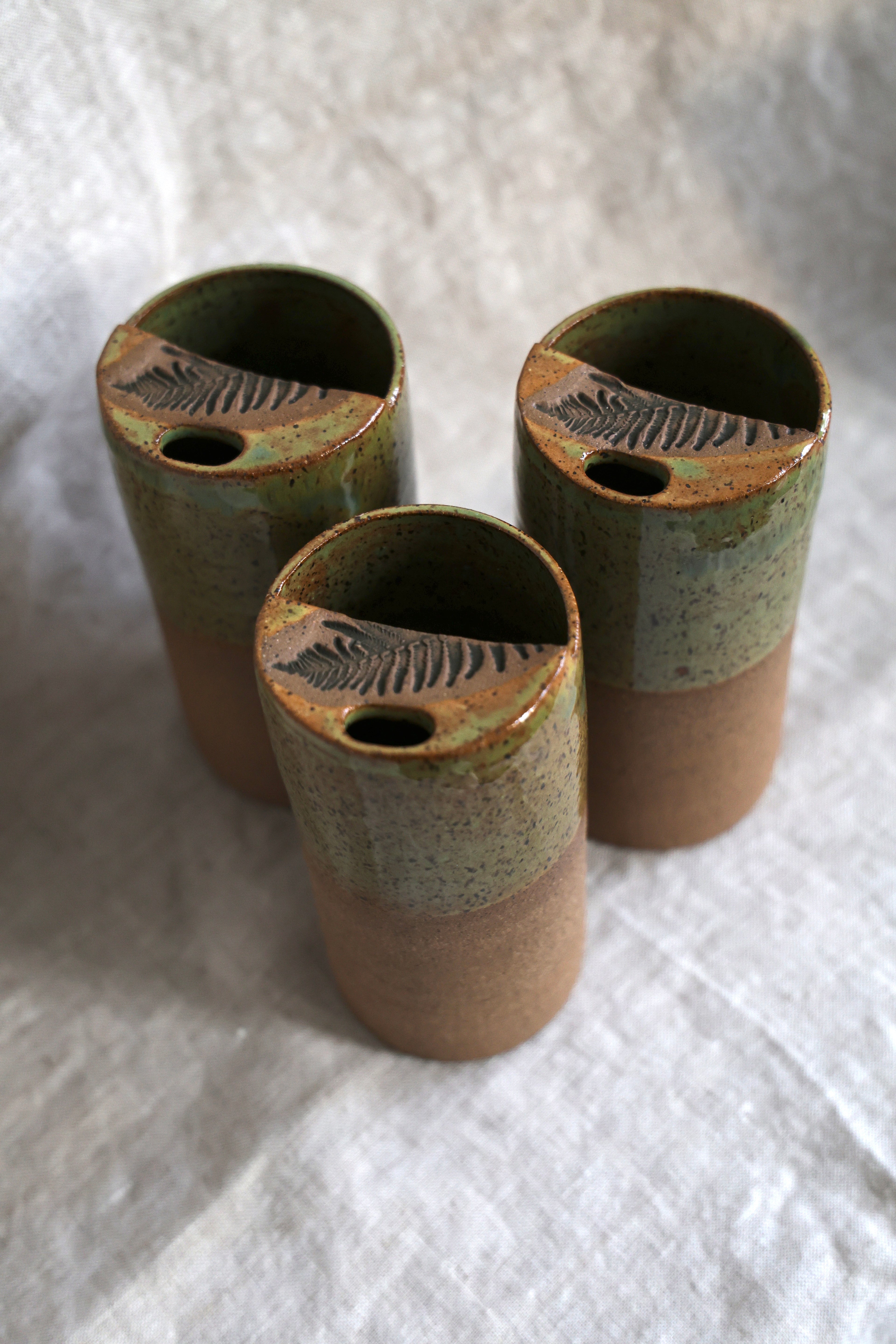 Three ceramic containers with fern patterns on a white fabric background