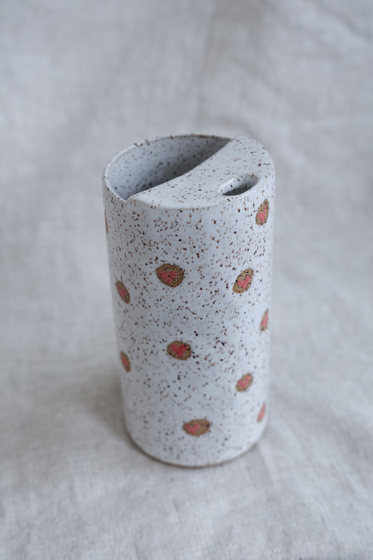 Speckled ceramic vase with pink hearts on a white fabric background