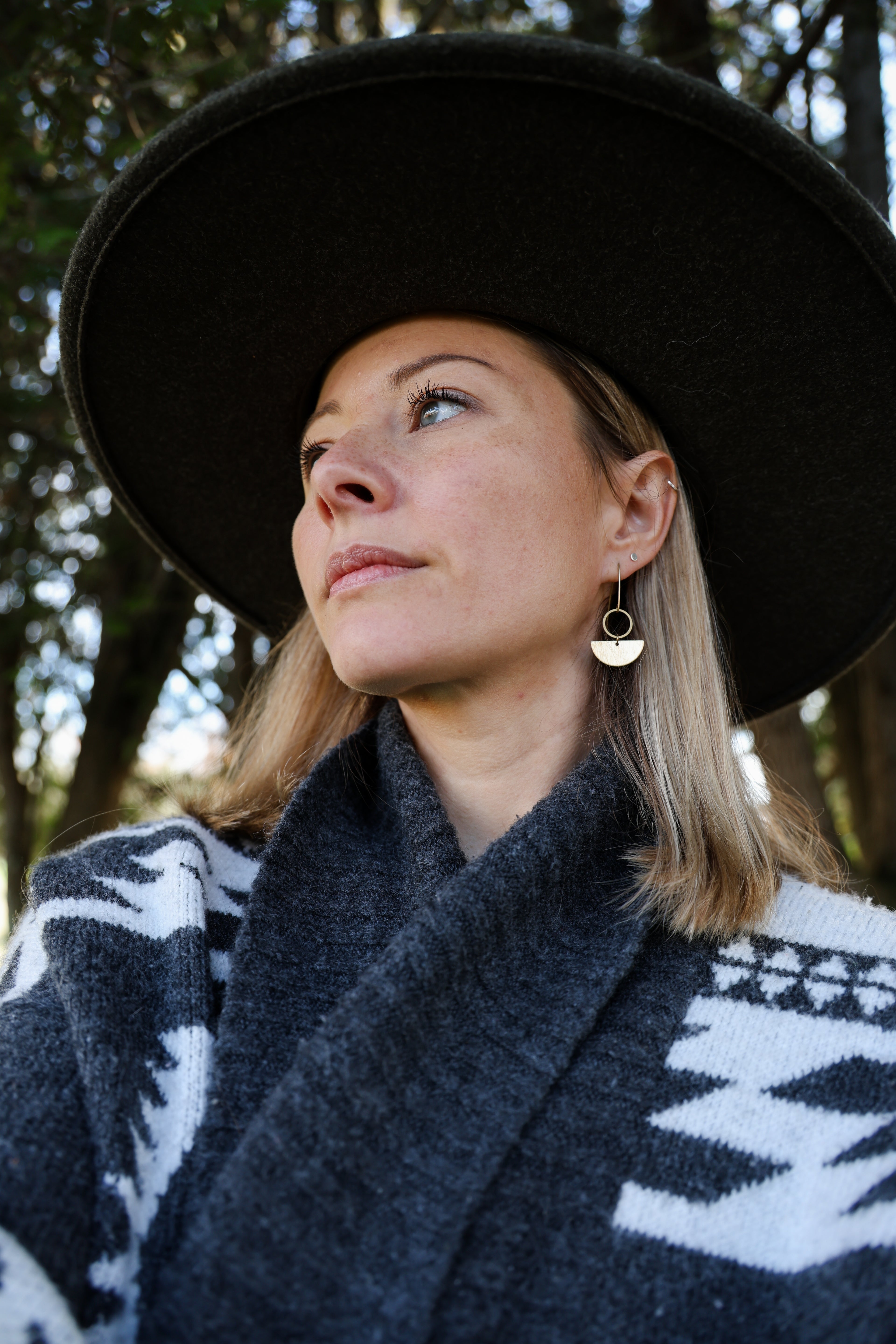 A person wearing a black hat and a geometric patterned garment, featuring gold-colored circular earrings.